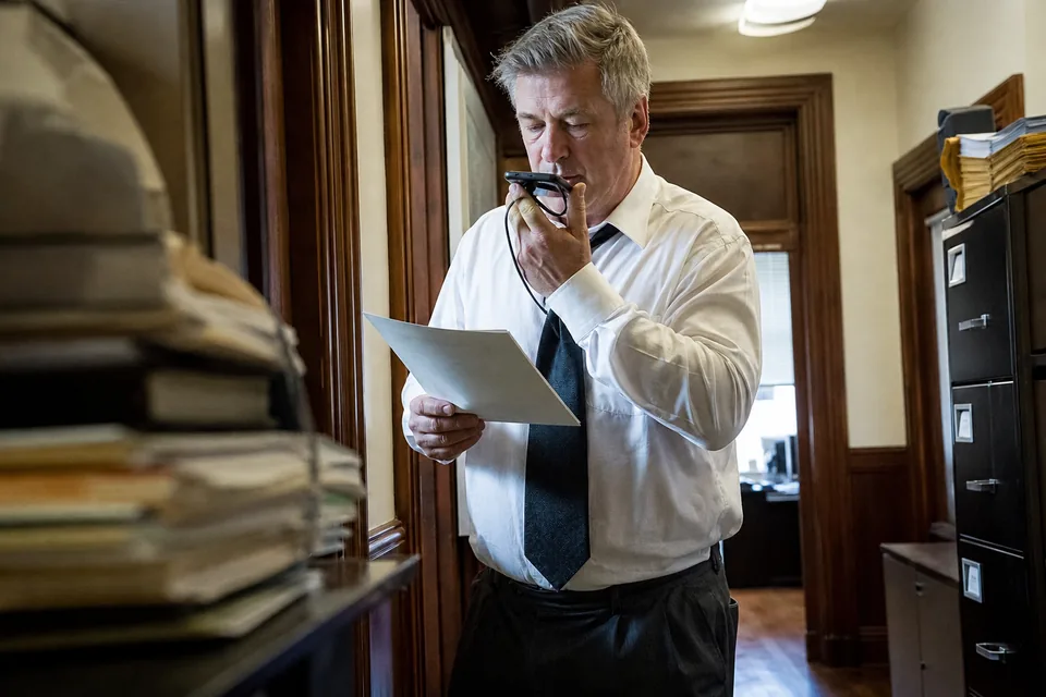 Attorney in a law office hallway, phone at his ear, dictating a reply between two calls