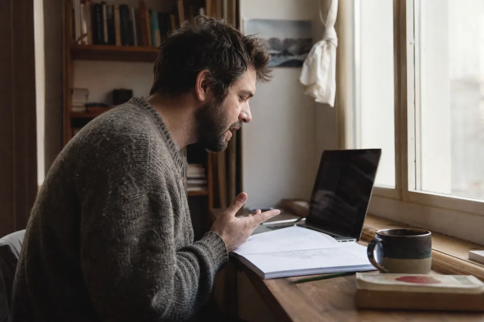 Writer dictating a draft at a window desk with printed notes and a cup of coffee